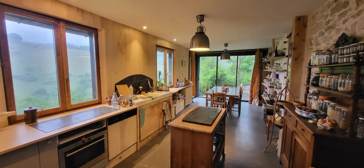 Grande cuisine en bois baignée de lumière, ouverte sur la salle à manger